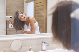 Brunette woman drying her hair upside down in front of a mirror